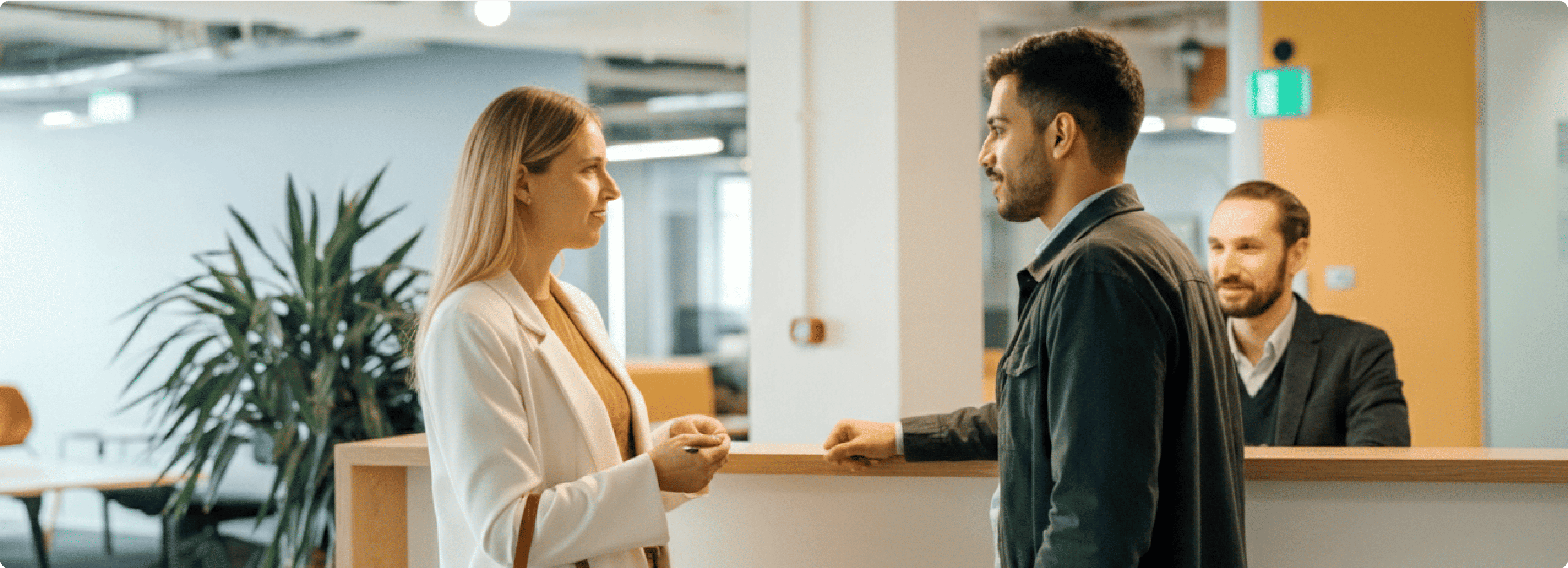 Two individuals engaged in conversation at a reception desk in a modern office environment.